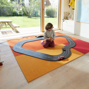 Teppich im Kinderzimmer - Ein Teppich in fröhlichen Farben liegt im Kinderzimmer. Ein Kind spielt darauf mit einer Rennbahn.