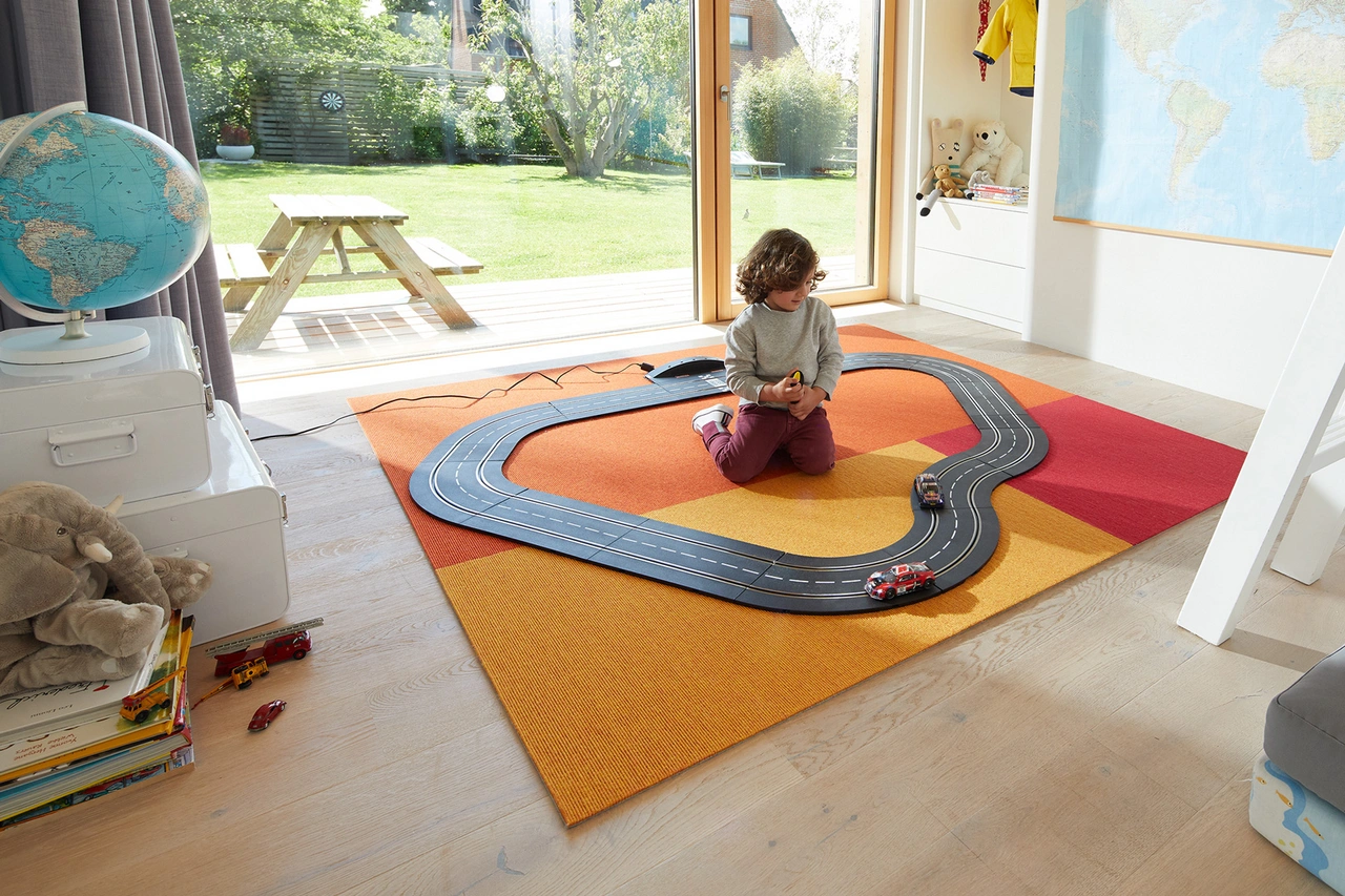 Ein Teppich liegt im Kinderzimmer. - Ein Teppich in fröhlichen Farben liegt im Kinderzimmer. Ein Kind spielt darauf mit einer Rennbahn.