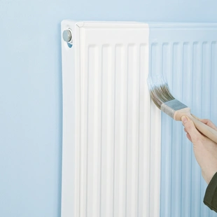 passender Lack zur Wand - Ein Heizkörper wird mit einem Pinsel in einer angemischten Farbe gestrichen.