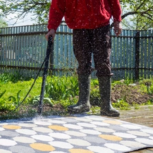 Ein Mann reinigt mit einem Wasserstrahl einen Outdoor Teppich in seinem Garten - Ein Mann reinigt mit einem Wasserstrahl einen Outdoor Teppich in seinem Garten
