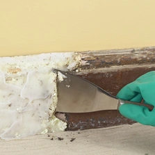 In jede Richtung - Mit Hilfe von Lösungsmitteln und einem Spachtel wird alte Farbe von einer Fußleiste entfernt.