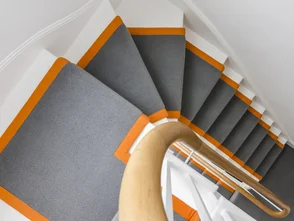 Maßgefertigter grauer Treppenläufer mit oranger Bandeinfassung auf weißer Treppe - Maßgefertigter grauer Treppenläufer mit oranger Bandeinfassung auf weißer Treppe