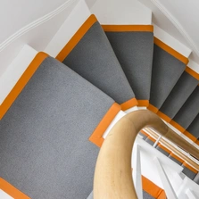 Maßgefertigter grauer Treppenläufer mit oranger Bandeinfassung auf weißer Treppe - Maßgefertigter grauer Treppenläufer mit oranger Bandeinfassung auf weißer Treppe