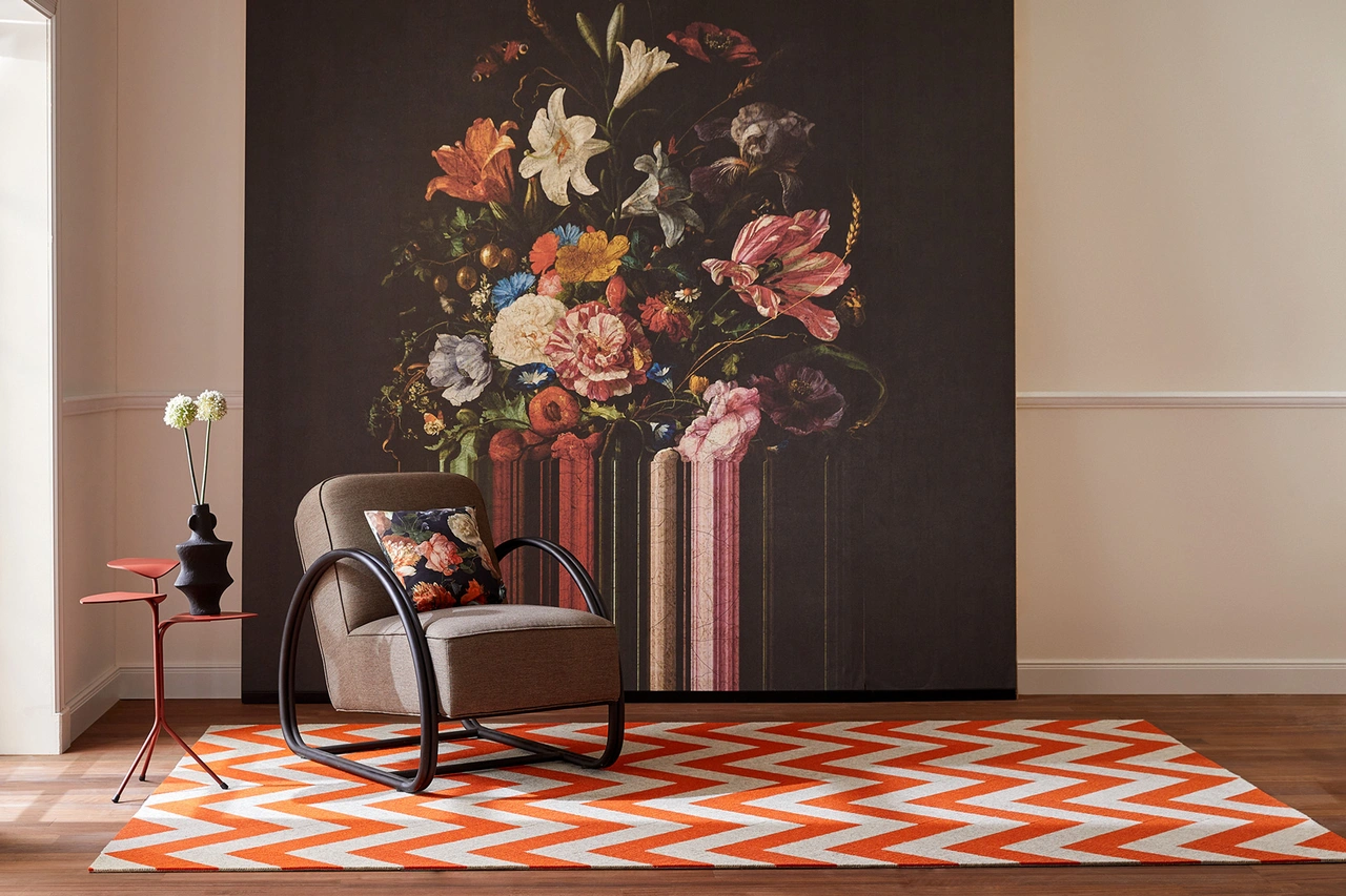 Illustration - Ihr Experte für schönes Wohnen - Ein orange beiger im Zickzack gemusterter Teppich liegt im Raum, im Hintergrund eine florale Tapete.