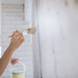 feste Untergründe - Junge Frau streicht mit einem Pinsel Tapetengrund zur besseren Haftung der Tapete auf eine Wand.