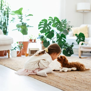Illustration - Ihr Experte für schönes Wohnen - Kleines Mädchen, das mit Hund spielt, im Wohnzimmer auf einem Naturfaserteppich.