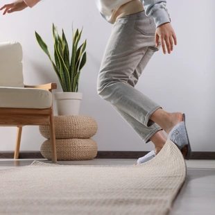 Illustration - Ihr Experte für schönes Wohnen - Frau stolpert zu Hause über Teppich, Nahaufnahme.