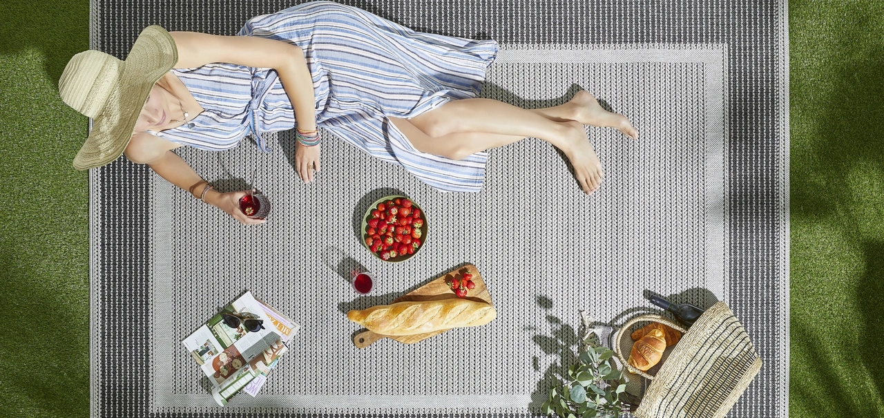 Eine Frau, sommerlich gekleidet, liegt auf einem Outdoorteppich auf einer Grünfläche mit einem Picknick. - Eine Frau, sommerlich gekleidet, liegt auf einem Outdoorteppich auf einer Grünfläche mit einem Picknick.