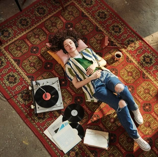 Illustration - Ihr Experte für schönes Wohnen - Mädchen in Freizeitkleidung, das auf dem roten, klassischem Teppich im Wohnzimmer liegt und Musik hört