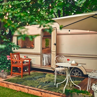 Ein Outdoor Teppich der in einer grünen Landschaft vor einem Wohnwagen liegt. - Ein Outdoor Teppich der in einer grünen Landschaft vor einem Wohnwagen liegt.