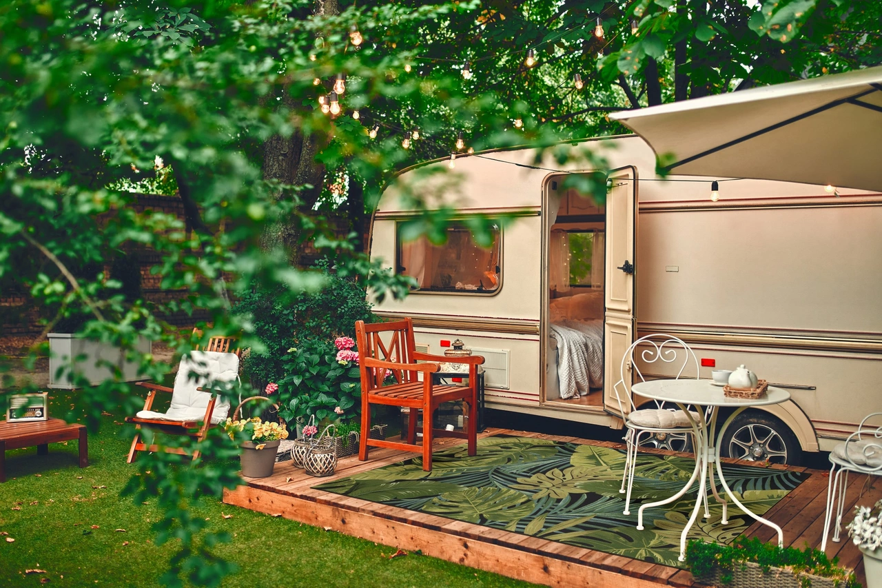 Ein Outdoor Teppich der in einer grünen Landschaft vor einem Wohnwagen liegt. - Ein Outdoor Teppich der in einer grünen Landschaft vor einem Wohnwagen liegt.